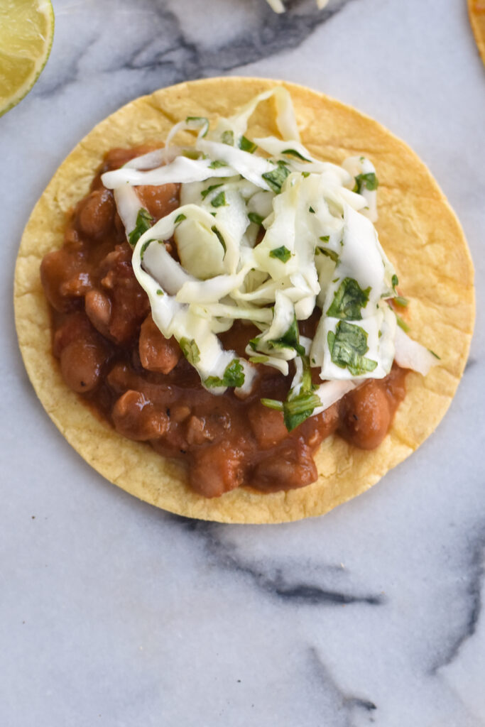 This Mexican bean recipe for tacos starts with chile infused pinto beans served in a warm corn tortilla topped with an easy, light refreshing slaw. 